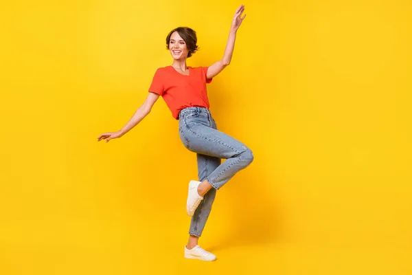 Full size foto van mooie brunette optimistische dame dans dragen rode t-shirt jeans sneakers geïsoleerd op levendige gele kleur achtergrond — Stockfoto