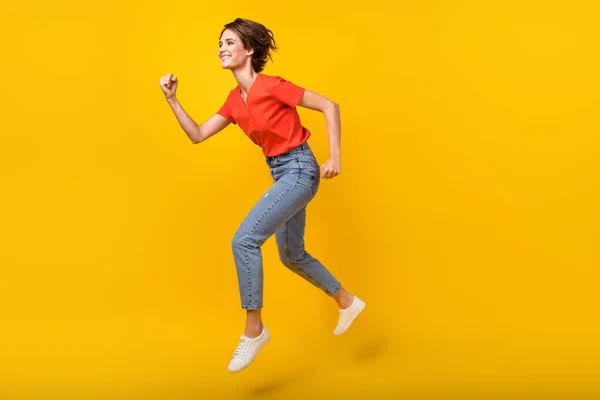 Foto de perfil de tamaño completo de la fresca morena optimista dama salto desgaste rojo camiseta jeans zapatillas aisladas en el fondo de color amarillo — Foto de Stock