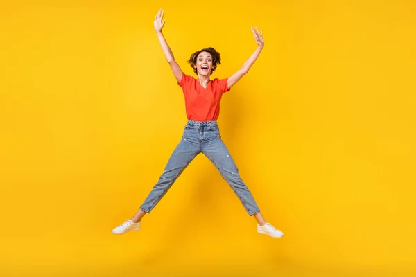 Foto de tamaño completo de la fresca morena optimista dama salto desgaste rojo camiseta jeans zapatillas aisladas en el fondo de color amarillo —  Fotos de Stock