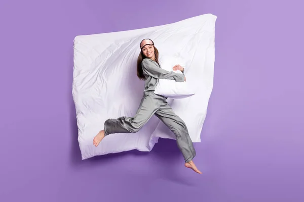 Volledige lengte body size foto van meisje springen op bed knuffelen kussen in grijze pyjama geïsoleerde pastel paarse kleur achtergrond — Stockfoto