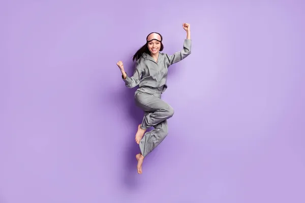 Ganzkörpergröße Foto von Mädchen springen tragen Pyjama Schlafmaske gestikuliert wie Sieger isoliert pastellvioletten Farbhintergrund — Stockfoto