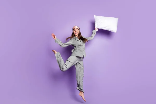 全身上下尽收眼底的漂亮时髦、快乐、无忧无虑的女孩抱着枕头跳跃，在紫色背景下与外界隔绝 — 图库照片