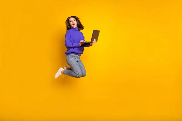 Πλήρες μέγεθος προφίλ πλευρά φωτογραφία του νεαρού χαρούμενα ενθουσιασμένοι κορίτσι άλμα με φορητό υπολογιστή σε χέρια απομονώνονται σε κίτρινο χρώμα φόντο — Φωτογραφία Αρχείου