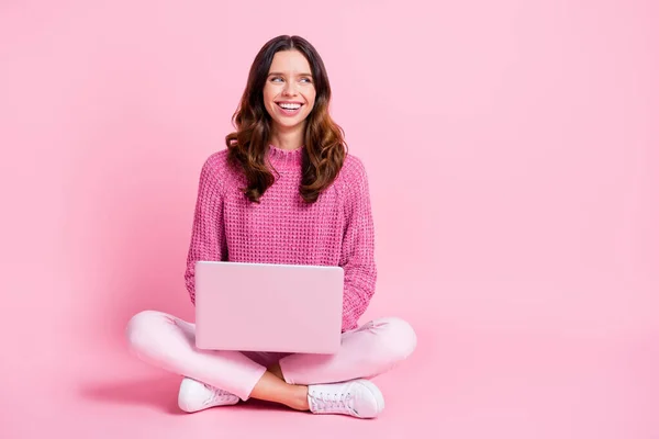 Фотография в полный рост оптимистичной симпатичной брюнетки, сидящей на ноутбуке, выглядит как пустое место в розовых брюках, изолированных на розовом фоне — стоковое фото