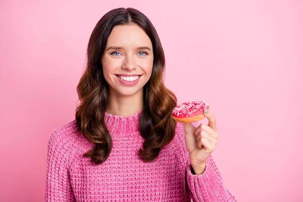 Portrait of attractive cheerful wavy-haired girl eating fresh baked doughnut isolated over pink pastel color background — Stock Photo, Image