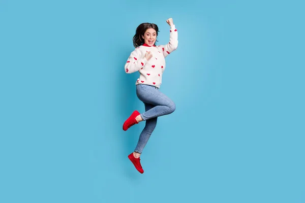 Фотографія повної довжини щасливої молодої жінки, одягнені в серця, друкує пуловер, стрибає з високими кулаками, ізольований синій колір фону — стокове фото