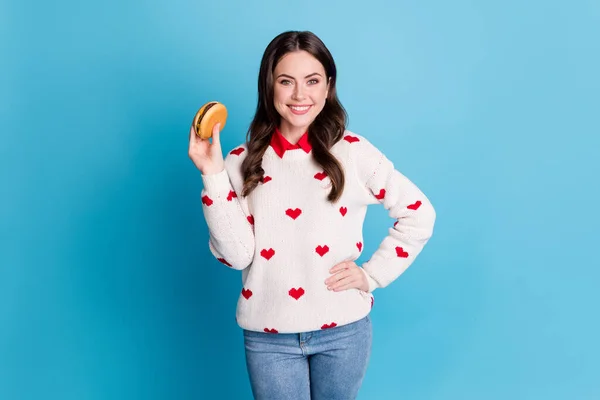 Fénykép aranyos édes fiatal nő öltözött szív nyomtatás pulóver eszik gazdaság sajtburger elszigetelt kék szín háttér — Stock Fotó