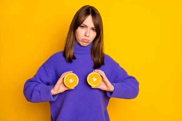 Photo of pretty upset young lady dressed violet sweater holding orange fruit parts cover tits isolated yellow color background — стоковое фото