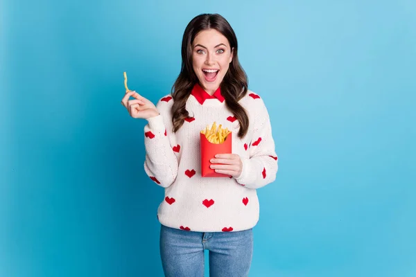 Foto av förvånad ung kvinna klädd hjärtan tryck pullover äta pommes frites läppar öppen mun isolerad blå färg bakgrund — Stockfoto