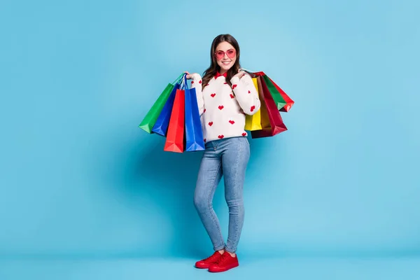 Ganzes Foto von junger Frau gekleidet Herzen drucken Pullover Brille hält Einkaufstaschen isoliert blaue Farbe Hintergrund — Stockfoto
