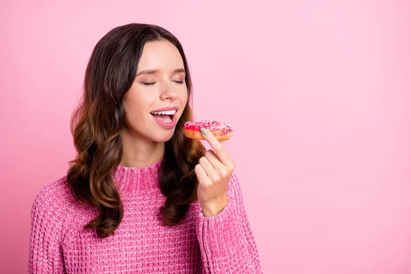 Retrato de atraente sonhador menina ondulada mordendo fresco assado donut cópia espaço isolado sobre cor pastel rosa fundo — Fotografia de Stock