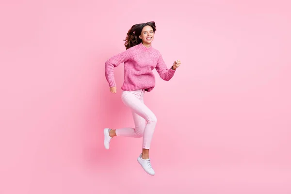フルサイズプロフィール写真の楽観的なクールなブルネットの女性のジャンプ実行はピンクの色の背景に隔離されたピンクのセーターパンツスニーカーを着用 — ストック写真