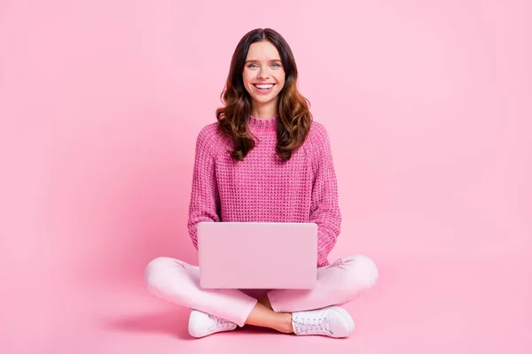 Pełny rozmiar zdjęcie optymistyczne miło brunetka pani siedzieć typ laptop nosić różowy sweter trampki izolowane na różowym tle — Zdjęcie stockowe