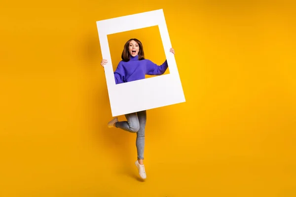 Ganzkörpergröße Ansicht von attraktiven fröhlichen Mädchen springen hält großen Papierrahmen Spaß isoliert über helle gelbe Farbe Hintergrund — Stockfoto