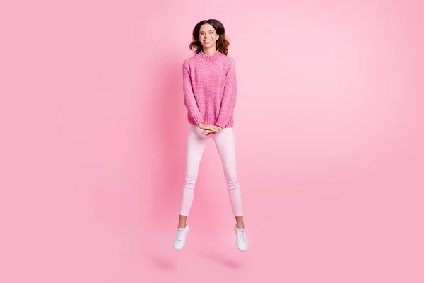 Foto de tamaño completo de optimista morena fresca dama salto usar suéter rosa pantalones zapatillas aisladas sobre fondo de color rosa —  Fotos de Stock
