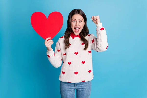 Foto de encantadora sorte jovem senhora usar corações impressão suéter segurando grande papel coração levantando punho isolado azul cor fundo — Fotografia de Stock