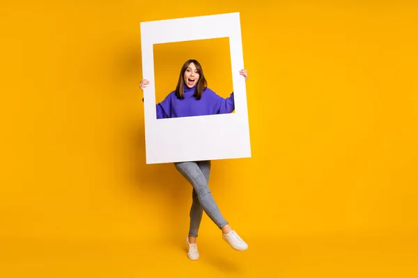 Mor renkli kazak giymiş parlak, genç bir bayanın fotoğrafı. Elinde fotoğraf çerçevesi, izole edilmiş turuncu arka plan. — Stok fotoğraf