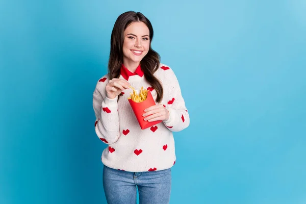 Foto de linda adorable joven dama usar corazones impresión suéter comer comida rápida papas fritas aislado color azul fondo — Foto de Stock