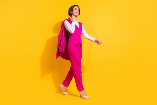 Foto de jovem mulher doce sonhador vestido terno rosa sorrindo andando espaço vazio isolado cor amarela fundo — Fotografia de Stock