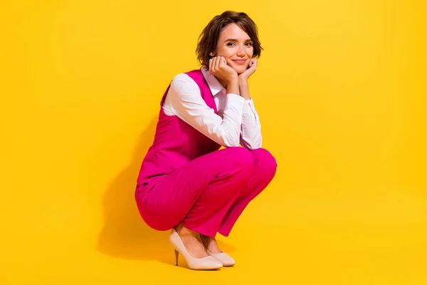 Fotografie okouzlující zasněný mladá žena oblečená růžová oblek usměvavé sedící ruce tváře izolované žlutá barva pozadí — Stock fotografie