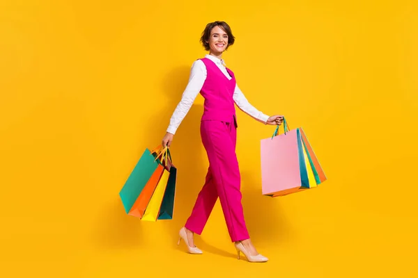 Photo of sweet shiny young woman dressed pink suit holding shopping bags walking isolated yellow color background — Stock Photo, Image