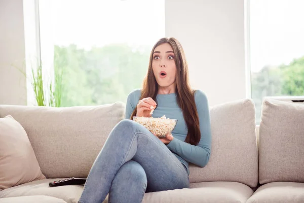 Фотопортрет молодой женщины, смотрящей фильм ужасов, сидящей на тренере и поедающей попкорн — стоковое фото