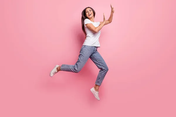 Foto de perfil de tamaño completo de la joven morena impresionada salto dama usar zapatillas vaqueros camiseta aislada sobre fondo rosa — Foto de Stock