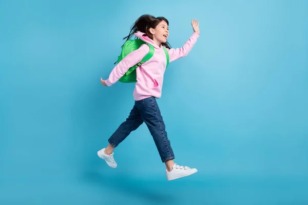 Foto de divertida colegiala amigable vestido rosa traje mochila caminando brazo agitando espacio vacío sonriendo aislado color azul fondo — Foto de Stock