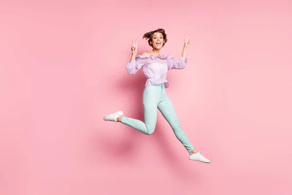 젊고 행복하고 흥분 한 긍정적 인 소녀의 전체 크기 사진 핑크 색 배경에서 고립된 v-sign 을 보여 주는 점프 — 스톡 사진