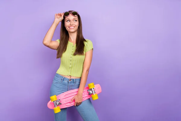 Portret van aantrekkelijke vrolijke meisje aanraken specs houden skate ponder kopiëren ruimte geïsoleerd over paarse paarse kleur achtergrond — Stockfoto