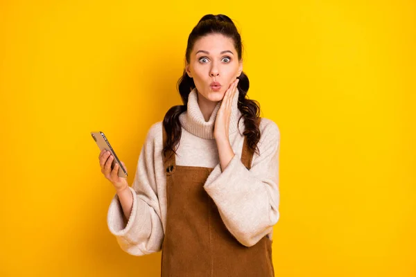 Foto van mooie brunette onder de indruk krullend kapsel dame houden telefoon hand gezicht slijtage trui geïsoleerd op gele kleur achtergrond — Stockfoto