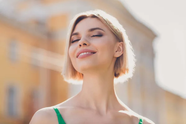 Foto de dulce adorable joven dama usar traje verde sonriendo caminando ojos cerrados disfrutando del sol fuera de la calle urbana de la ciudad —  Fotos de Stock