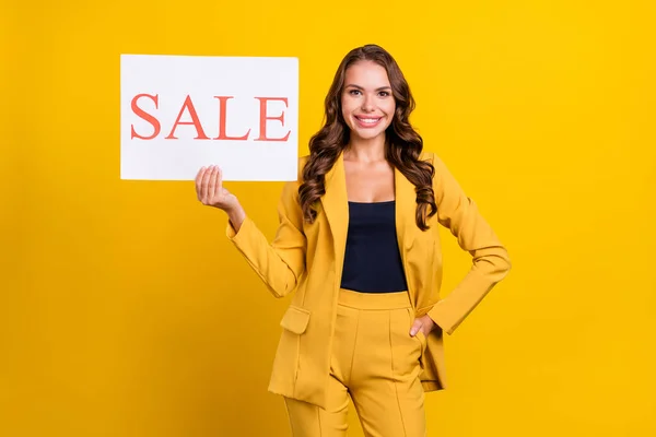 Foto van mooie aantrekkelijke jonge vrouw gekleed pak blazer glimlachen holding verkoop plakkaat geïsoleerde gele kleur achtergrond — Stockfoto