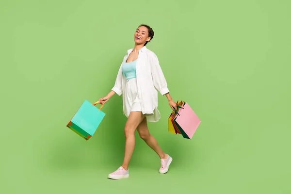 Πλήρες μήκος σώματος μέγεθος φωτογραφία γυναίκα κρατώντας τσάντες περπάτημα στο εμπορικό κέντρο απομονωμένο παστέλ πράσινο χρώμα φόντο — Φωτογραφία Αρχείου