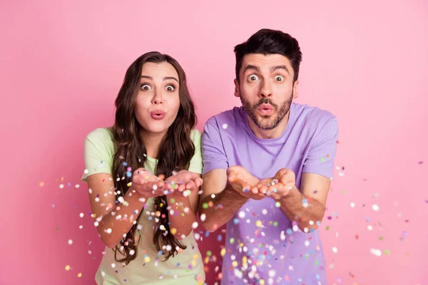 Portrait of attractive funny couple blowing decorative elements having fun free time isolated over pink pastel color background — Stockfoto
