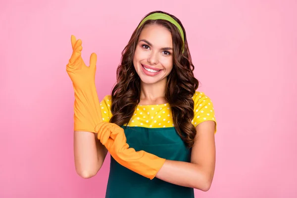 Фото мрійливої солодкої молодої леді, одягненої в зелений фартух помаранчеві рукавички готові прибирати усміхнений ізольований рожевий колір фону — стокове фото