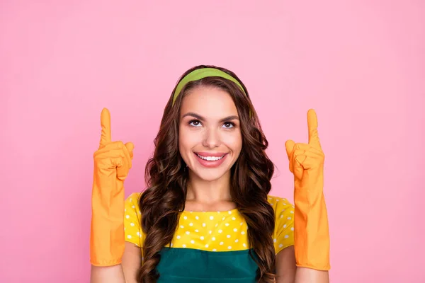 Фото очаровательной юной леди, одетой в зеленый фартук резиновые перчатки, выглядящие указывая пустое пространство улыбаясь изолированный розовый цвет фона — стоковое фото