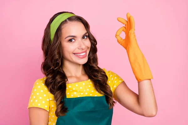 Фото очаровательной милой юной леди, одетой зеленый фартук резиновые перчатки показывая okey знак улыбаясь изолированный розовый цвет фона — стоковое фото