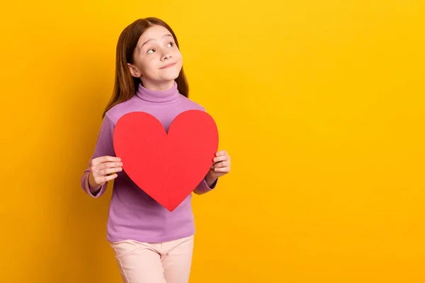 Foto de feliz positivo sonhador encantador doce menina olhar copyspace segurar vermelho coração de papel isolado no fundo de cor amarela — Fotografia de Stock