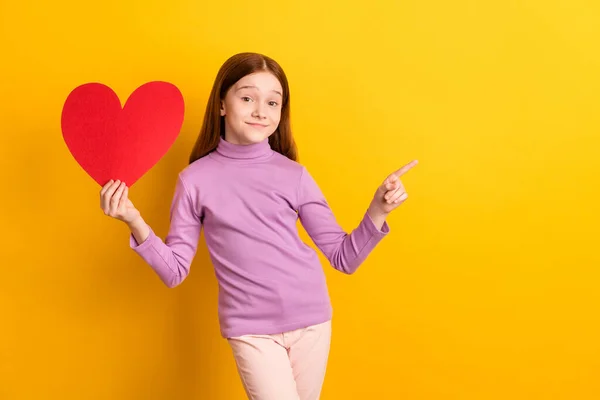 Retrato de bela menina alegre na moda segurando em mãos grande cartão de coração mostrando espaço de cópia isolado sobre fundo de cor amarelo brilhante — Fotografia de Stock