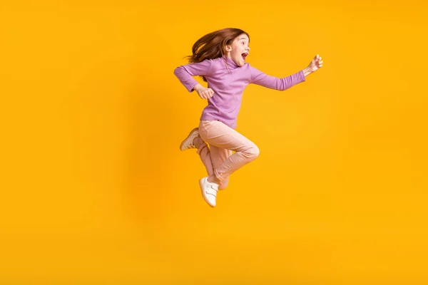 Фотография счастливой взволнованной веселой улыбающейся маленькой девочки, бегущей в воздухе на желтом цветовом фоне профиля в полный рост — стоковое фото