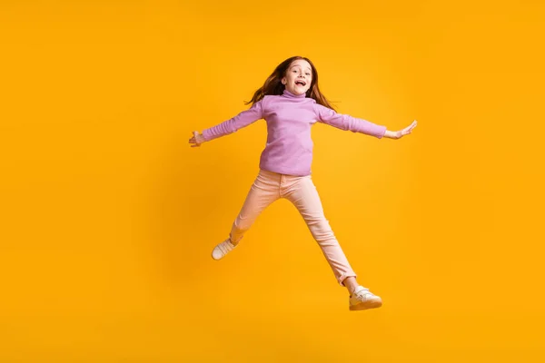 Фотография в полный рост со счастливым хорошим настроением взволновала маленькую девочку, прыгающую весело на желтом цветовом фоне — стоковое фото
