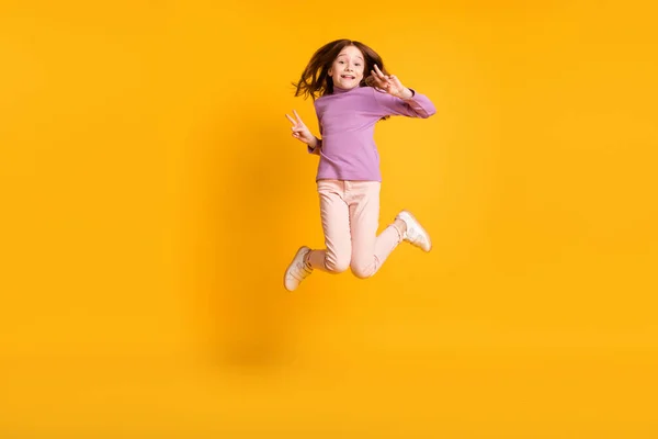 Foto de tamaño completo de feliz emocionado positivo sonriente niña saltando mostrar v-signo aislado en el fondo de color amarillo —  Fotos de Stock