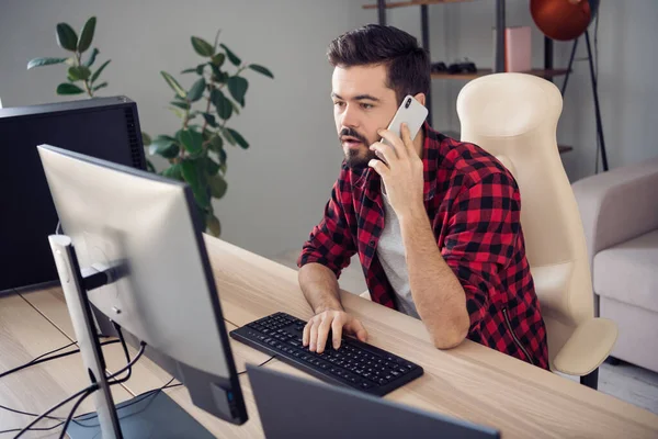 Fotografie seriózního mladého muže psát počítačový programátor držet telefon mluvit uvnitř kanceláře pracoviště — Stock fotografie