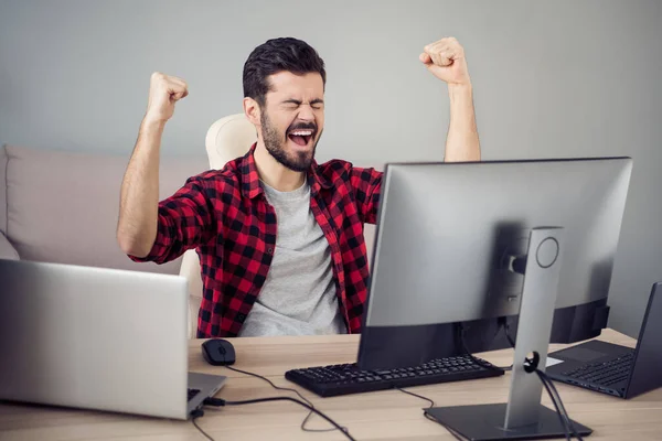 Фото веселый счастливый сумасшедший молодой человек празднуют победу сидеть стол программиста работу в помещении офиса на рабочем месте — стоковое фото