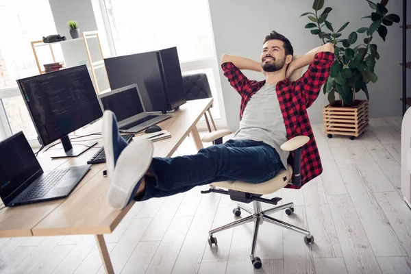 Портрет привлекательного веселого мечтательного парня-техника, сидящего в кресле, отдыхающего в конце дня в помещении офиса — стоковое фото