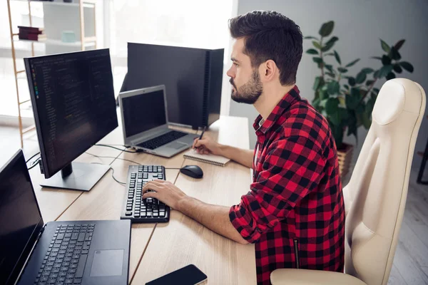 Profil Seite Foto von ernsthaften jungen Mann aussehen Bildschirm schreiben Code Web-Design sitzen Schreibtisch drinnen im Büro Arbeitsplatz — Stockfoto