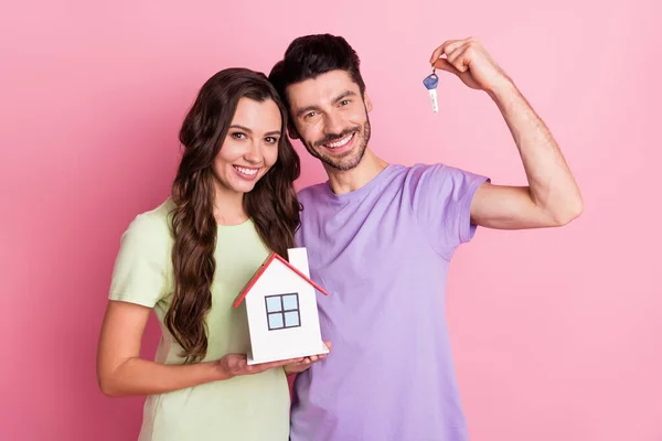 Πορτρέτο της υπέροχο χαρούμενο ζευγάρι αγκαλιάζει κρατώντας στα χέρια νέο σπίτι βασικό πιστωτικό δάνειο που απομονώνονται σε ροζ παστέλ χρώμα φόντο — Φωτογραφία Αρχείου