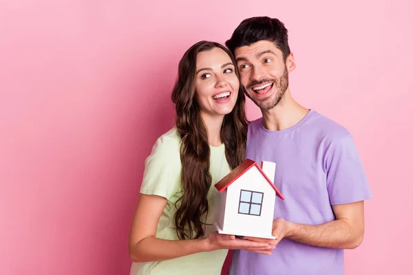 Retrato de pareja alegre atractiva abrazando la celebración de la casa mirando a un lado préstamo de crédito de espacio de copia aislado en el fondo de color rosa —  Fotos de Stock