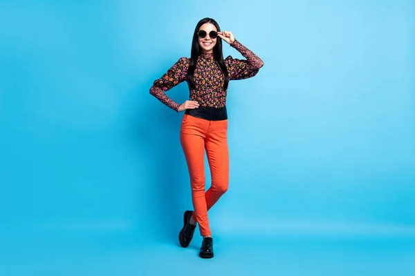 Foto van zelfverzekerde dame poseren look camera dragen retro specs bloem print shirt broek laarzen geïsoleerde blauwe kleur achtergrond — Stockfoto